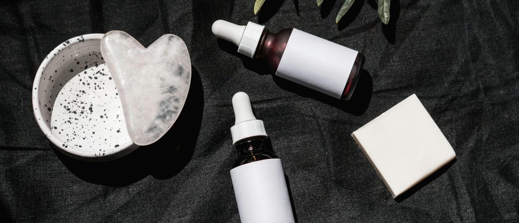 brown glass bottles on black textile beside gua sha and leaves