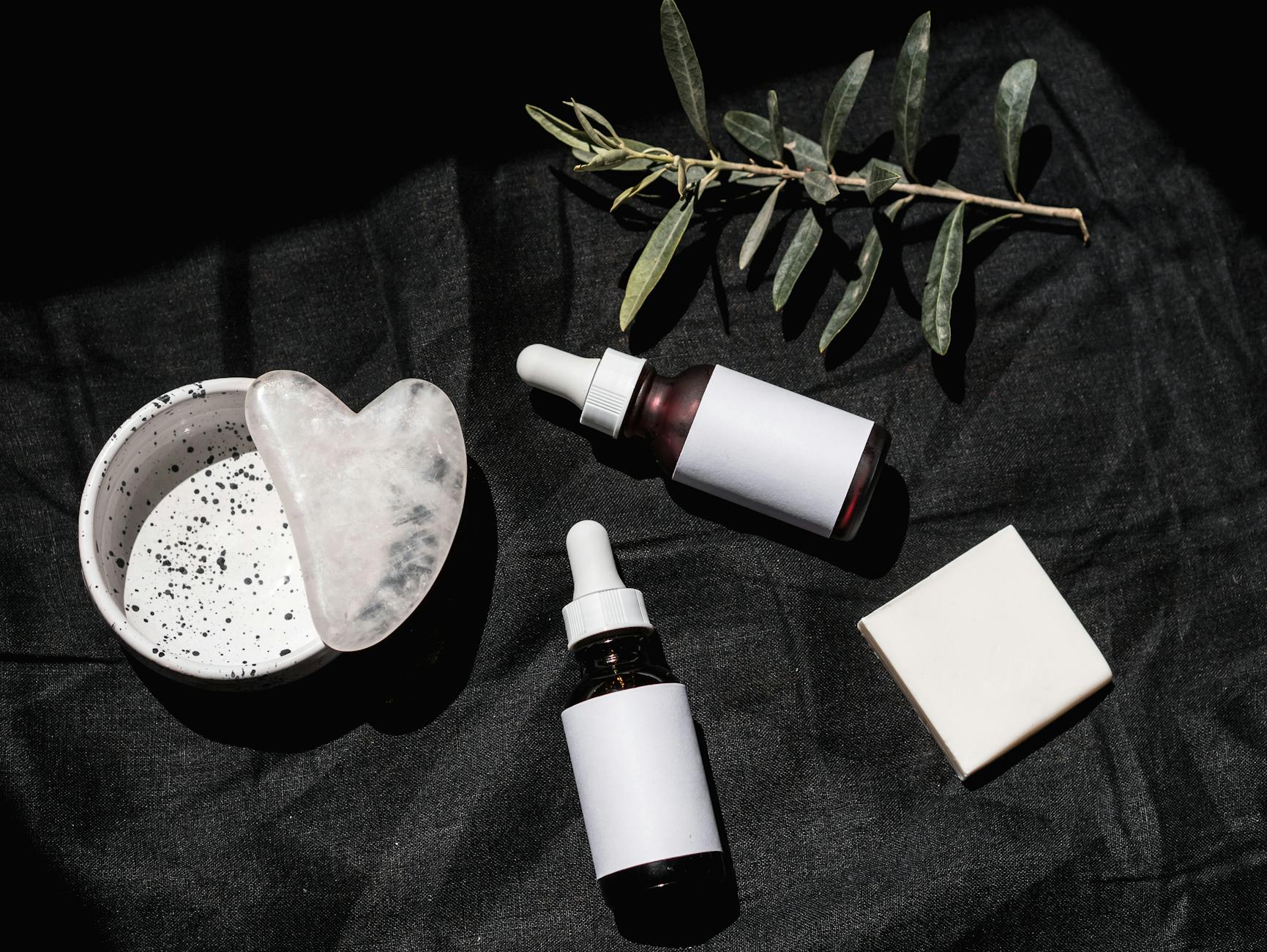 brown glass bottles on black textile beside gua sha and leaves